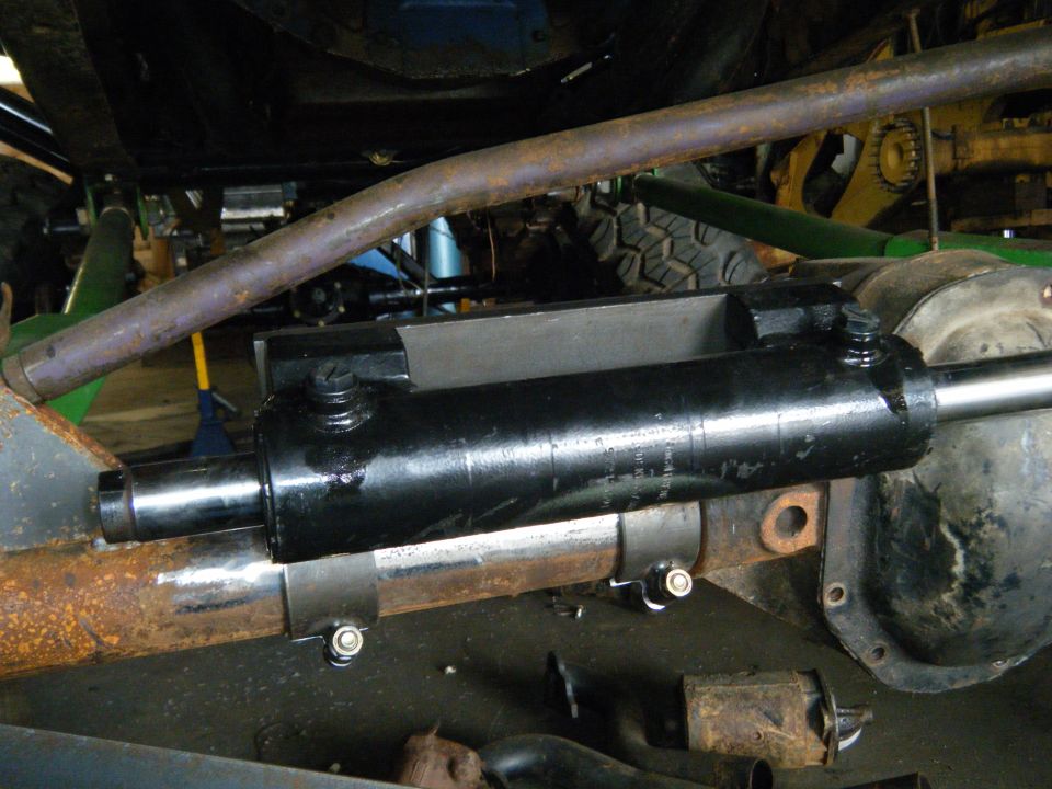 Hydraulic steering cylinder attached to a rusty axle housing, with suspension components visible