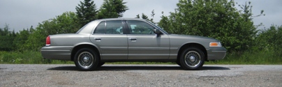 1999 Ford Crown Victoria - Side view of a gray Ford Crown Victoria sedan parked outdoors.
