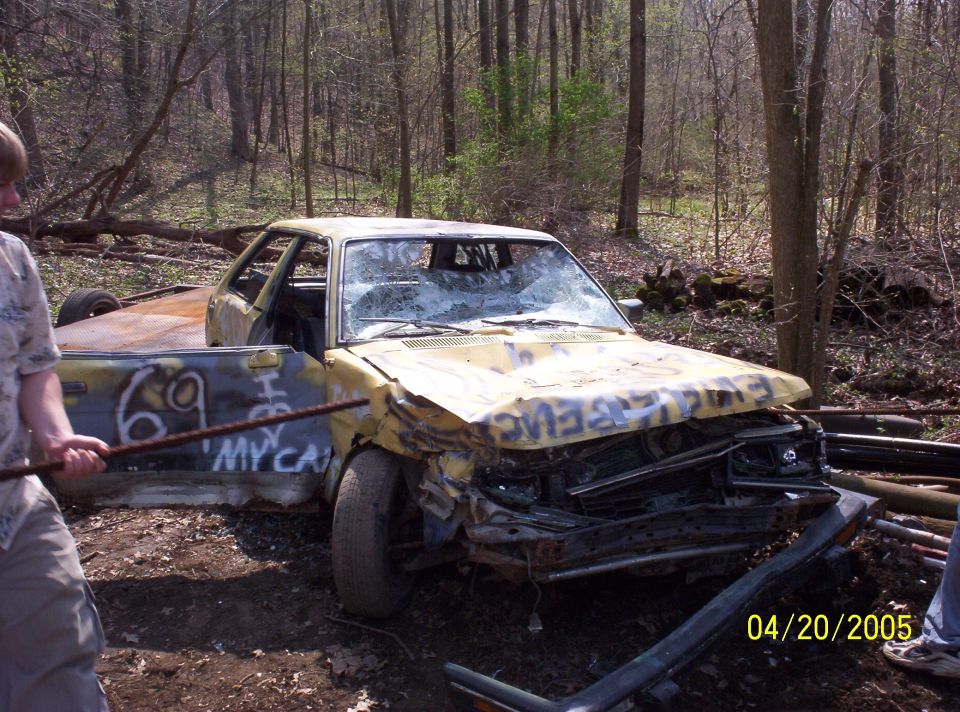 Yellow car with graffiti, broken windshield, and damaged front end