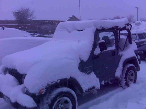 2008 Jeep Wrangler - A Jeep Wrangler is almost completely covered by a thick layer of snow, with another vehicle nearby also snow-laden.