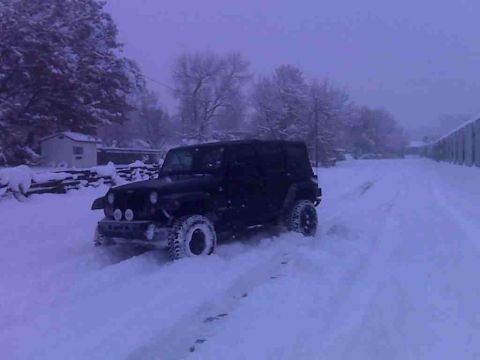 2008 Jeep Wrangler - A black 2008 Jeep Wrangler navigates a snow-covered road, kicking up powder as it drives.