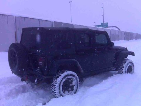 2008 Jeep Wrangler - Jeep Wrangler struggling in heavy snowfall on a road with a concrete barrier.