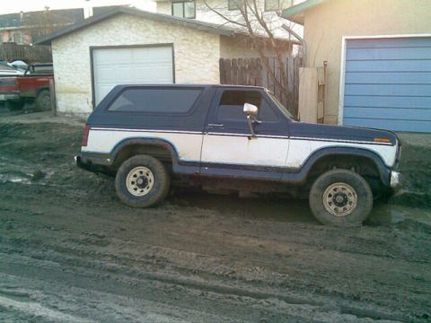 1985 Ford Bronco - This two-tone Ford Bronco is seen from the side, stuck in muddy terrain.
