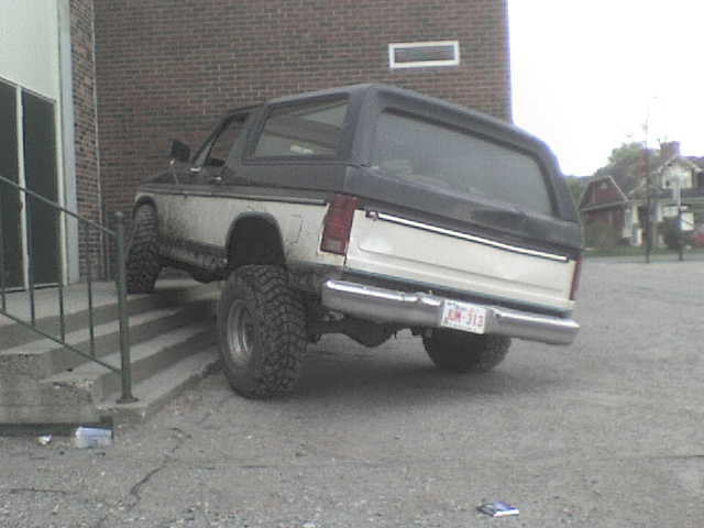 1985 Ford Bronco parked on a gravel lot next to a brick building, rear view