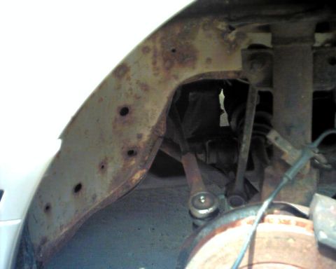 1990 Ford Taurus - Close-up view of a heavily rusted wheel well and suspension components, with a Supermotors.net watermark.