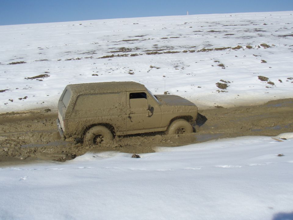 Mud-covered 1985 Ford Bronco stuck in mud with snow in background