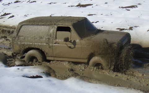 1985 Ford Bronco - Muddy 1985 Ford Bronco struggling through a treacherous, snow-dusted mire.