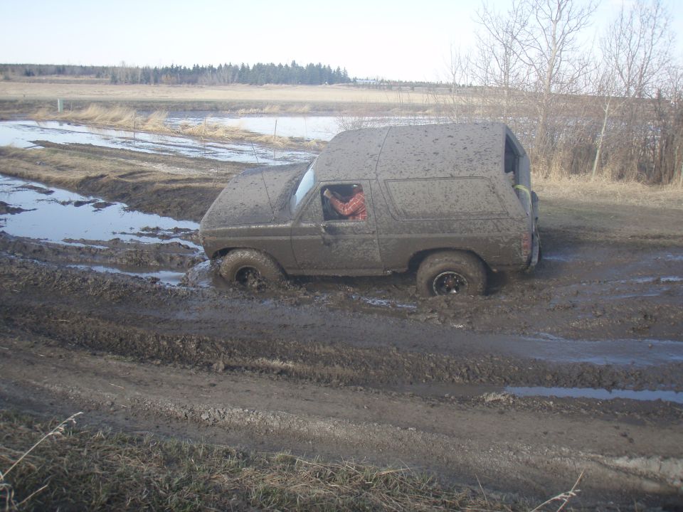 Muddy SUV stuck in a muddy field. Driver visible inside
