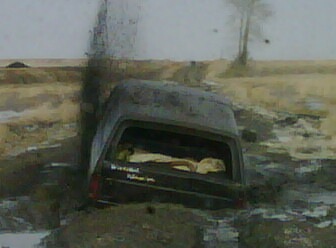 1985 Ford Bronco - A dark-colored SUV is deeply stuck in muddy terrain, with smoke billowing from its rear.
