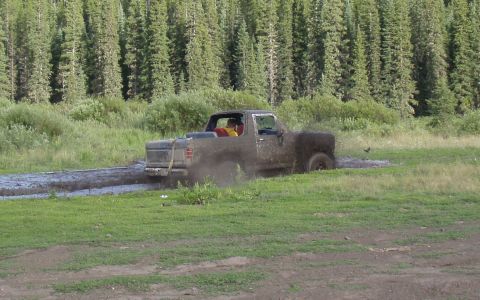 1985 Ford Bronco - A pickup truck navigates a muddy trail, kicking up dirt and water.