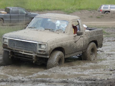 1985 Ford Bronco - Muddy pickup truck struggling in a mud pit with other vehicles nearby.
