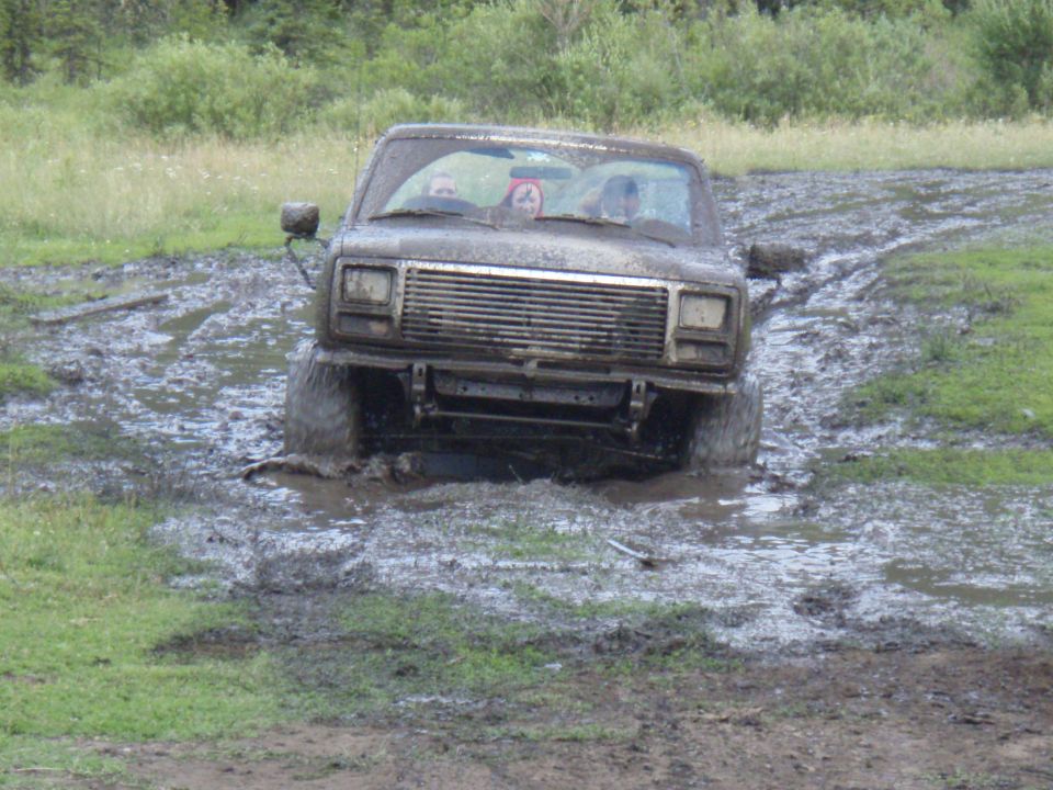 Mud-splattered SUV stuck in mud, front view. Grille and headlights visible