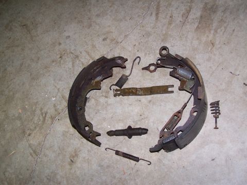 1991 Jeep Comanche - Disassembled drum brake assembly with rusty metal parts and springs on a concrete floor.