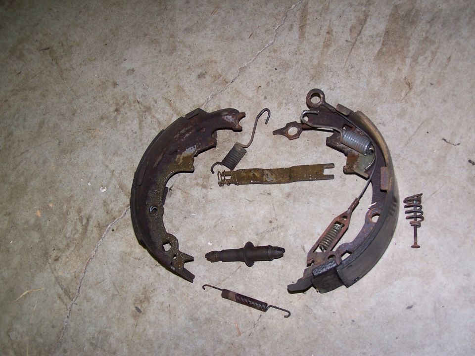 Disassembled drum brake assembly with rusty metal parts and springs on a concrete floor