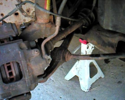 1990 Ford Taurus - Close-up view of a vehicle's suspension and brake system, with a jack stand providing support.