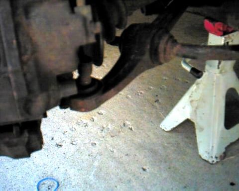 1990 Ford Taurus - Underbody view of a vehicle's front axle, control arm, and CV shaft resting on a white jack stand on concrete.