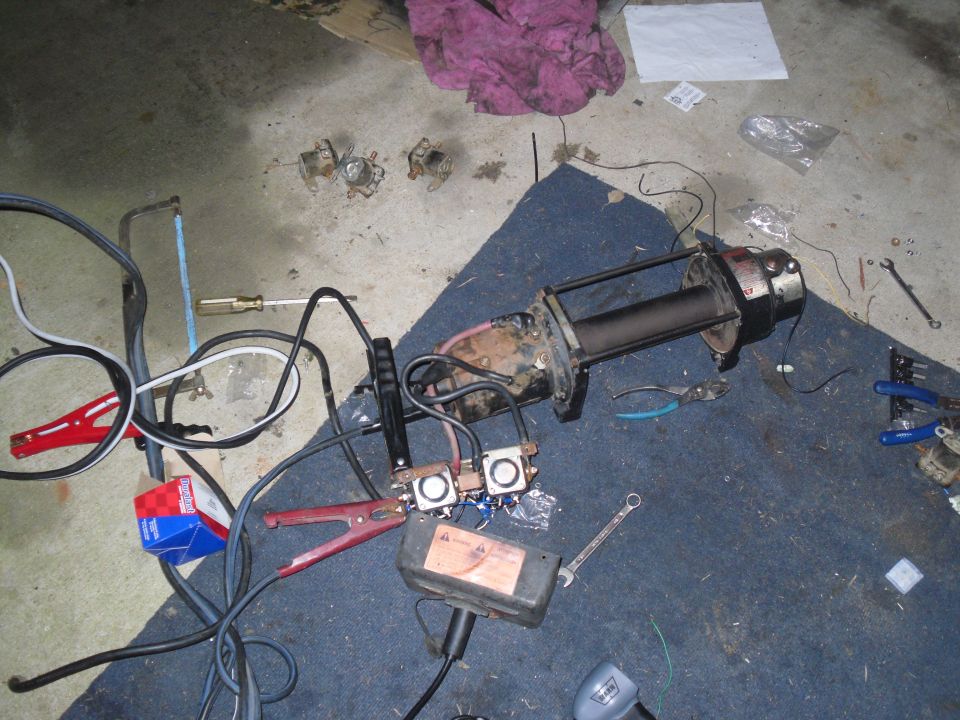 Disassembled electric winch with solenoids and battery cables on a garage floor