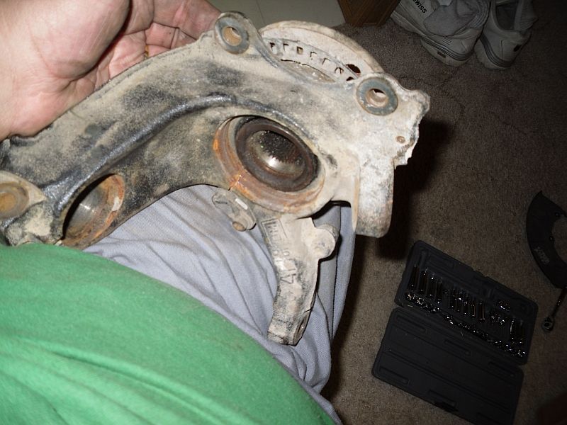 dirty car suspension knuckle with bearing and splines visible, held by a hand