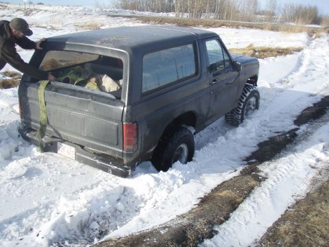 1985 Ford Bronco - Ford Bronco stuck in snow, with a person attempting to push it from behind.