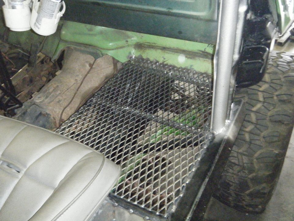 Interior of a vehicle with a metal grate floor, custom roll bar, and a light-colored seat. Some cans are mounted overhead