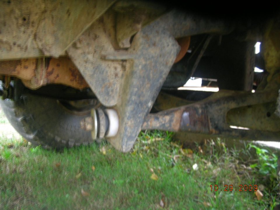 Under-truck view of rusty solid front axle, coil spring perch and radius arm