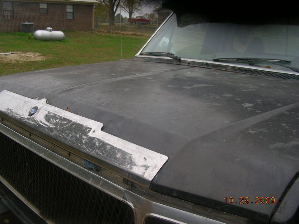 Pickup hood in gray primer with body filler on bare-metal front trim panel