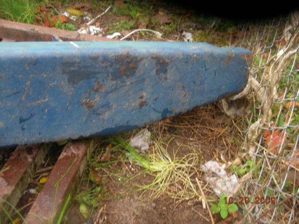 Weathered blue-painted metal object on wooden pallets by a chain-link fence