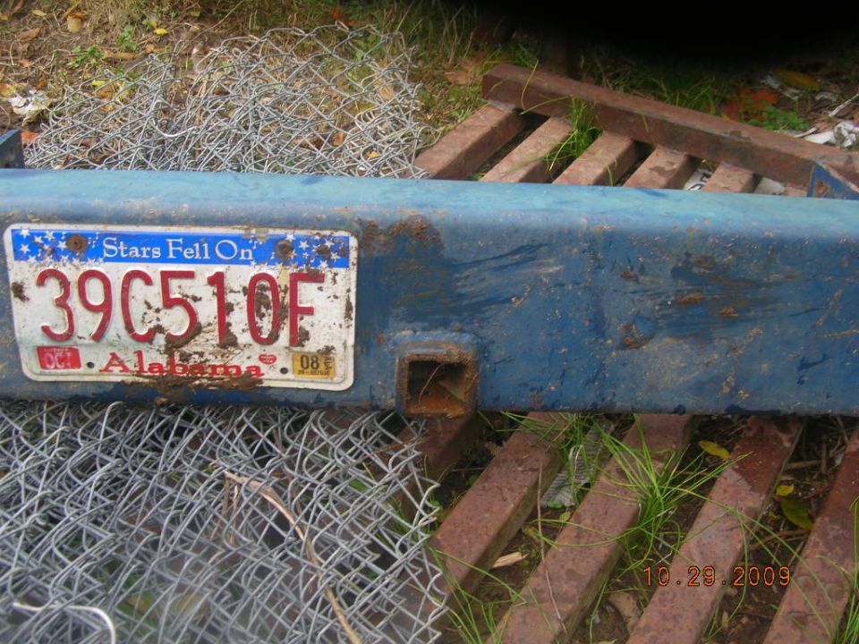 Rusty blue steel rear bumper with Alabama license plate lying in the grass