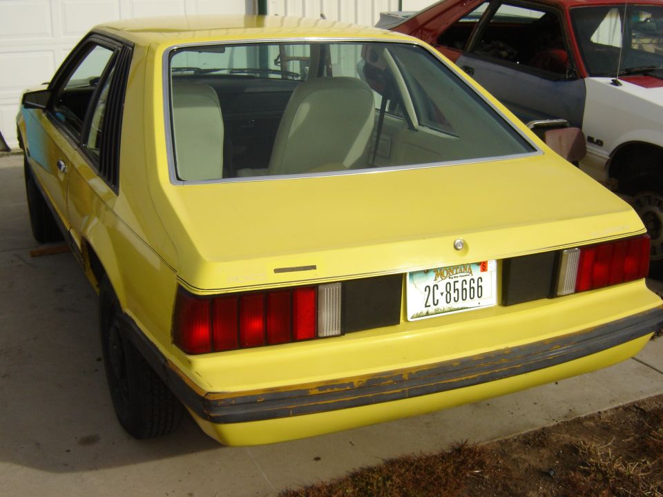 Yellow Fox-body Mustang hatchback, rear view, Montana plate 2C 85666, red Mustang behind
