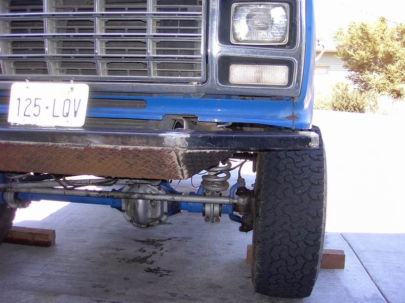 Blue Ford front axle and suspension viewed low, with grille, headlights and off-road tire.