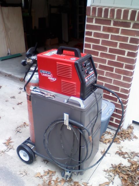 1996 Ford Bronco - Welding equipment, including a red Lincoln Electric welder and a gas tank, sits on a cart outdoors.