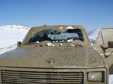 1985 Ford Bronco - This 1985 Ford Bronco is heavily covered in mud and snow, with another vehicle partially visible.