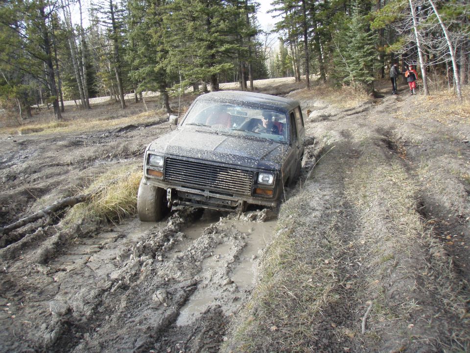 1985 Ford Bronco stuck in mud on a trail with trees in the background