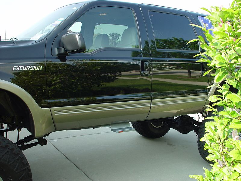 Black lifted Ford Excursion SUV shown in side profile on driveway