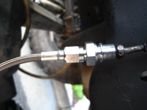 1989 Ford Bronco - A close-up view shows a braided brake line connected to a metal fitting, likely part of a vehicle's braking system.