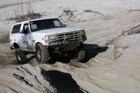1995 Ford Bronco - A white Ford Bronco navigates a sandy off-road course with a custom front bumper.