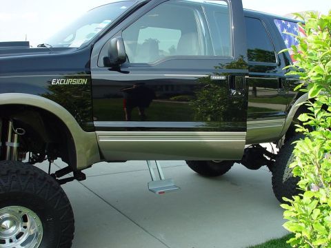 2001 Ford Excursion - A black Ford Excursion SUV is shown with a lifted suspension and large off-road tires. An American flag decal is visible on the rear window.