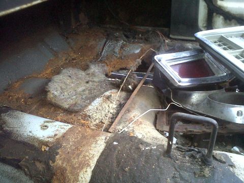 1973 Ford Ranchero - The interior floor pan of a vehicle shows significant rust and damage, with a taillight assembly visible.