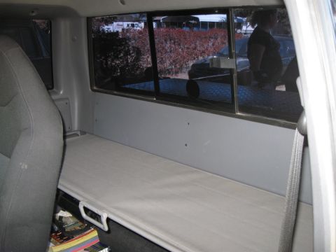 2003 Ford Ranger - The interior of a truck bed is shown with a cot set up and a stack of books on the floor.