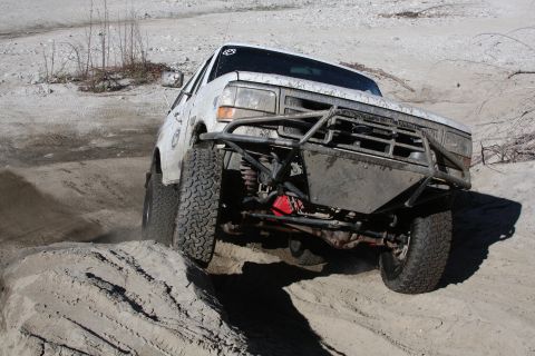 1995 Ford Bronco - This modified 1995 Ford Bronco navigates a challenging sandy terrain with its robust off-road enhancements.