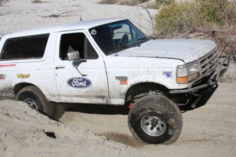 1995 Ford Bronco - White 1995 Ford Bronco navigating sandy terrain with modified bumper and off-road tires.
