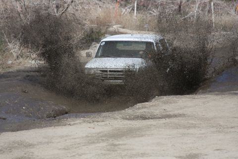 1995 Ford Bronco - A white SUV, likely from the early 1990s, navigates a muddy obstacle, creating a significant splash.