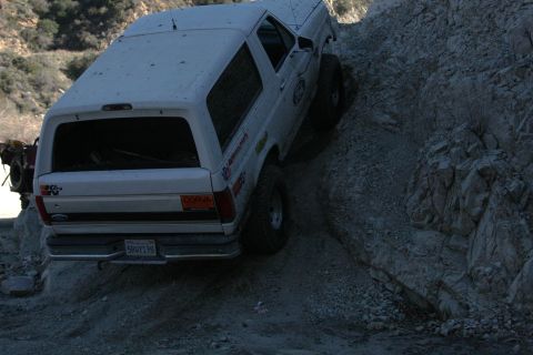 1995 Ford Bronco - White 1995 Ford Bronco navigating a challenging off-road path on a rocky slope.