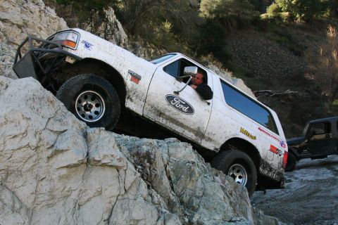 1995 Ford Bronco - A white Ford Bronco navigates a steep, rocky trail, with mud splattered on its body.