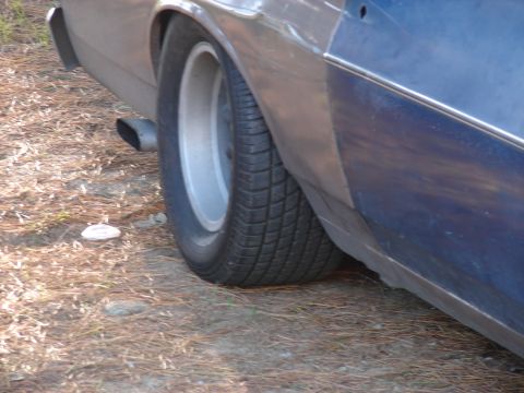 1973 Ford Ranchero - Close-up view of the rear wheel and quarter panel of a blue vehicle, showing the exhaust pipe and tire tread.
