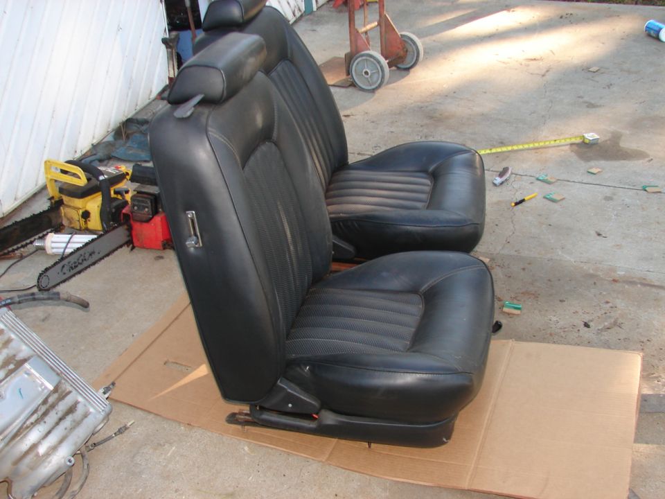 Black leather bucket seats with headrests, next to a chainsaw