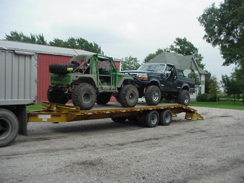 1992 Ford Bronco - Two modified off-road vehicles, a green buggy and a black Ford pickup, are transported on a trailer.