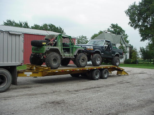 Green custom off-road buggy and black Ford F-150 pickup truck on a yellow car hauler trailer