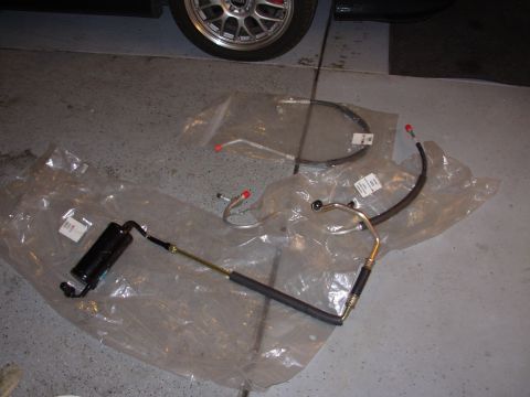 1995 Ford Taurus - Several power steering hoses and a reservoir are displayed on the floor, with a car wheel in the background.