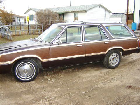 1984 Ford LTD - Station wagon with wood paneling, seen from the side in a dirt lot.
